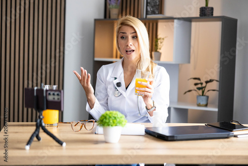Tableau sur toile Female doctor recording health tips and nutrition advice with smartphone, holdin