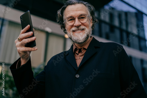 Happy senior executive with cellphone, cheerful male leader using high speed 5G internet for business communication in urban city environment, career growth, financial freedom, social media influencer