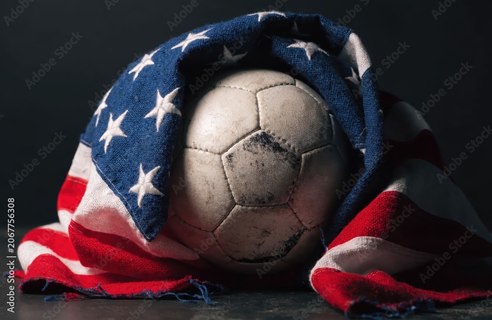 Obraz premium Vintage Soccer Ball Enveloped in a Tattered American Flag Representing Patriotism and the Spirit of US Soccer