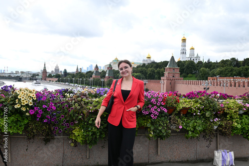 A beautiful blonde girl of European appearance stands and poses against the background of the Moscow Kremlin by the embankment