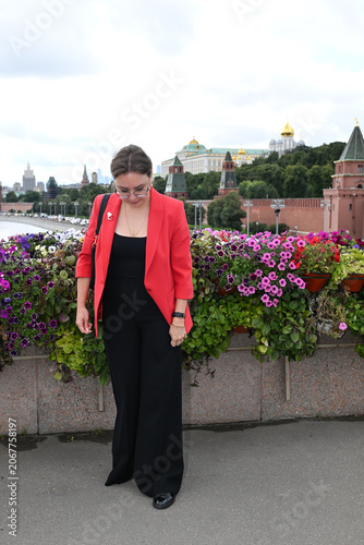 A beautiful blonde girl of European appearance stands and poses against the background of the Moscow Kremlin by the embankment