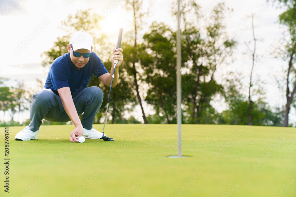 Obraz premium Male golfer placing and aiming golf ball on putting green