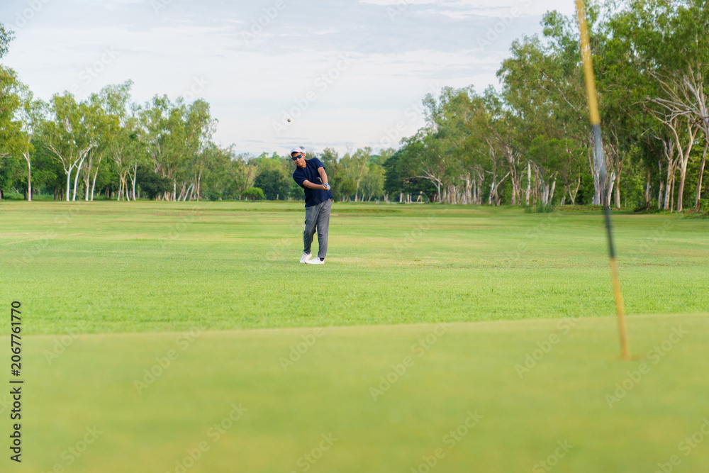 Obraz premium Distant view of an asian golfer hitting a ball towards the green.