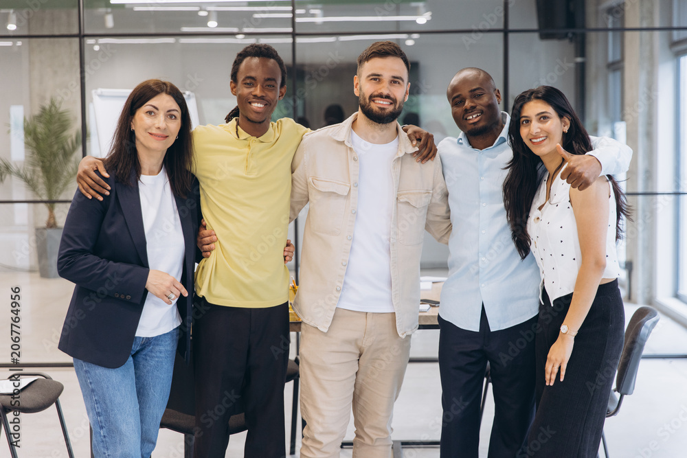 Fototapeta premium Diverse business team smiling, standing together in office, embracing teamwork and partnership for success