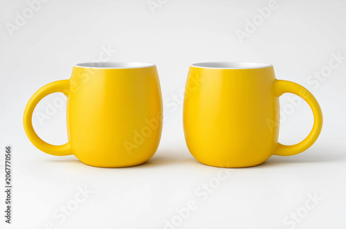 Two bright yellow ceramic coffee mugs facing each other on a light gray background