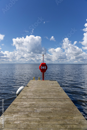 Wooden pier with red lifebuoy on calm sea under blue sky with clouds in Kuznica, Hel Peninsula, Poland
