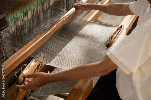 Konstfotografi Over the shoulder view of a skilled artisan operating a wooden handloom, weaving beautiful grey wavy patterned tenun fabric