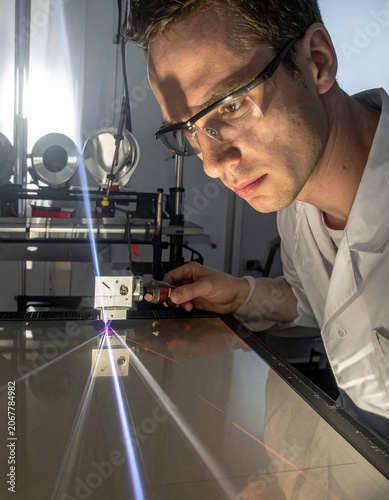 A researcher's hands adjust a precision laser beam on an optical table inside a dark laboratory for a light diffraction experiment.
