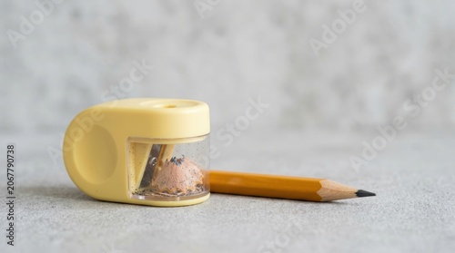 Pencil and Coin Bank on Gray Surface with Sharpener.