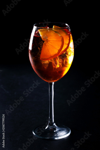 Refreshing cocktail with orange slices and ice in a glass on black background