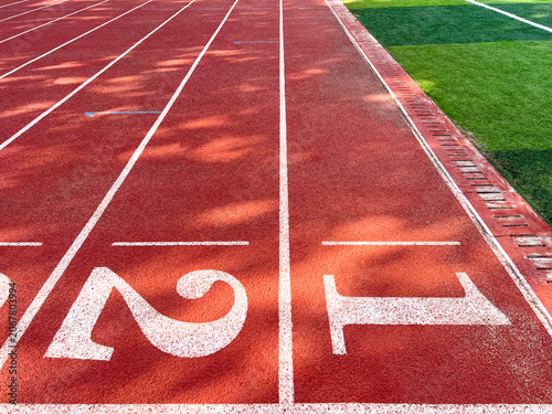 Red rubber running track lanes with start numbers 1, 2, 3 and adjacent green artificial grass field. Authentic outdoor stadium surface, ideal for racing, sports training, and competition backgrounds.