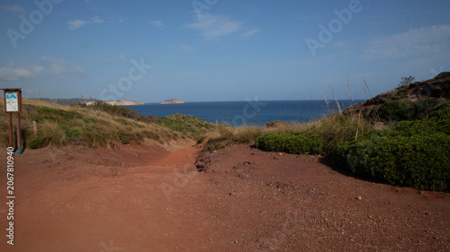 Dirt path leading to a scenic ocean view with green foliage