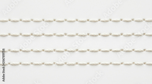 Close-up view of four parallel rows of white stitching on a white background, creating a textured pattern.