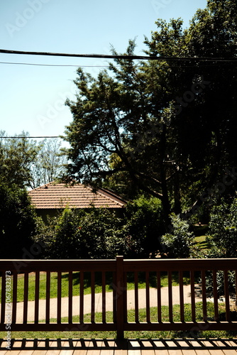 View from a Wooden Terrace Overlooking a Manicured Garden and Villa at a Peaceful Retreat in Sunny Garden Grounds with Lush Lawns and Tiled Roof Architecture Seen from a Deck