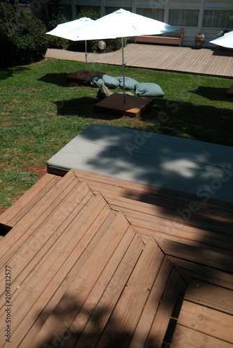 Peaceful Resort Lounge Setting at Outdoor Terrace with Wooden Deck and Shaded Lounge Area in a Sunny Garden Umbrellas