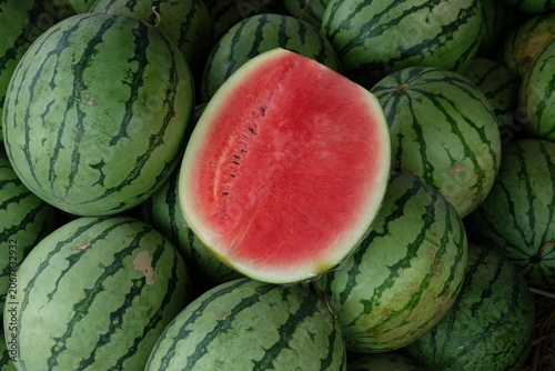 watermelon slices on top of a pile of watermelons at a fruit stand.