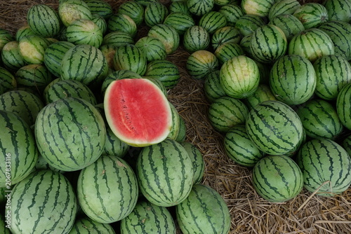 watermelon slices on top of a pile of watermelons at a fruit stand.