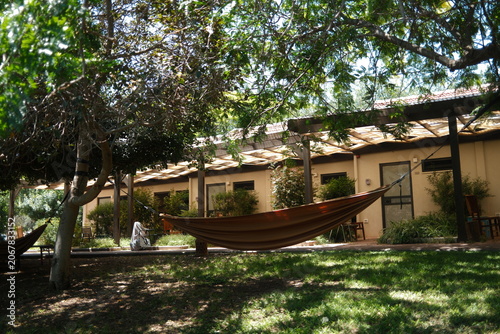 A Peaceful  Relaxing Hammock Strung Between Trees in a Serene Resort Garden Setting at An Inviting Outdoor Relaxation Space with Pergola-Covered Patio in the Background