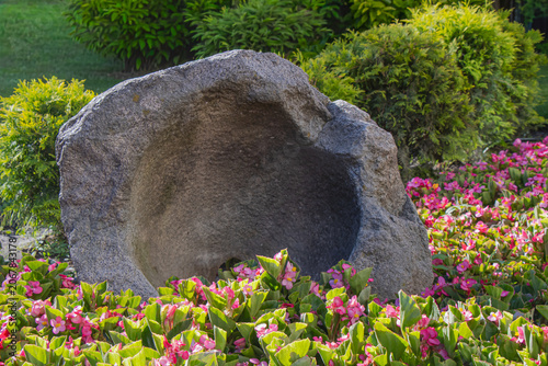 Ancient stone basin surrounded by pink flowers and green shrubs in a landscaped garden