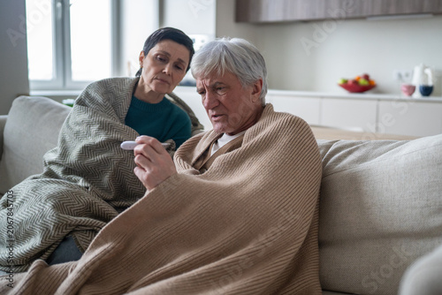Fotografija Exhausted elderly suffering from seasonal cold disease, husband checking tempera
