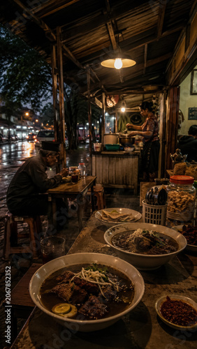 Bowl of rawon served inside a dark rustic night market stall with warm hanging lights .generative AI