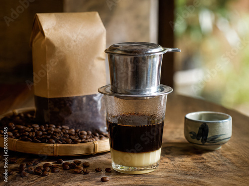 Vietnamese coffee drip beside roasted beans, kraft bags, and a small ceramic cup .generative AI