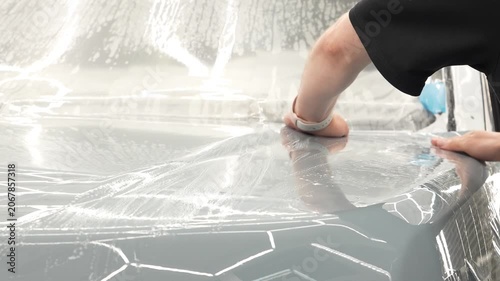 Car wrapping, detailing, tuning and styling. Selective focus. PPF protective film against chips and scratches. A car wrapping specialist applies a polyurethane film to the car. Detailer smoothes PPF. 