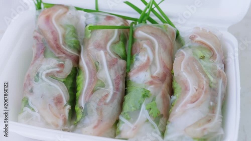 Fresh vietnamese summer rolls, known as gi cun, filled with pork ear, noodles, and fresh vegetables, slowly rotating in a white takeout container for a delicious culinary presentation
