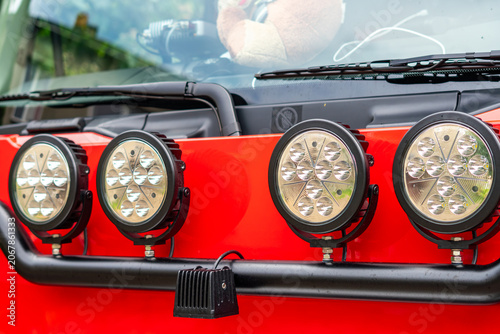 Fotografie Four round auxiliary LED headlights mounted on a black bull bar on the front of a red truck or off-road vehicle, showing the windshield, wipers, and a plush toy inside