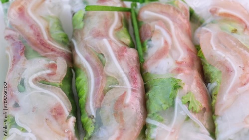 Authentic vietnamese summer rolls with pork ear, fresh herbs, and rice vermicelli noodles wrapped in translucent rice paper slowly rotating on a white plate, showcasing a traditional appetizer