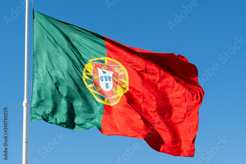 Quadro su tela Large national flag of Portugal waving in the wind against a vibrant blue sky background