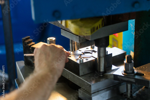Industrial press stamping metal components in factory workshop. Close-up of manufacturing detail and production process