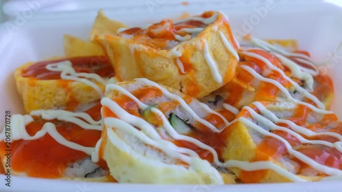 Fresh japanese sushi rolls wrapped in an egg omelette and garnished with spicy chili sauce and mayonnaise, served in a white takeout container for a quick and savory meal or appetizer