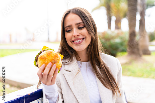 Tableau sur toile Young pretty woman holding a burger at outdoors with happy expression