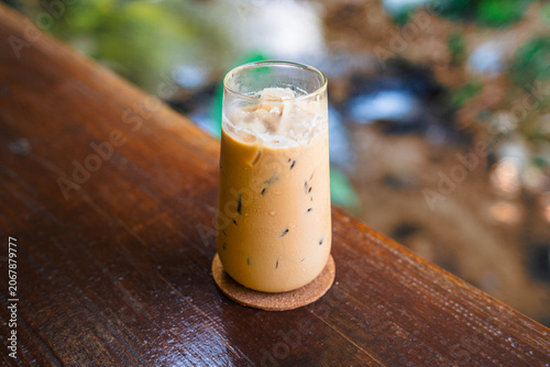 Iced espresso coffee glass on a wooden counter with a scenic nature background
