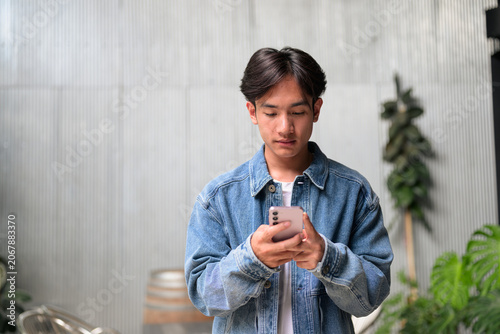 Young Asian non-binary man using phone by corrugated wall wide