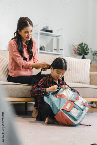 Fotografie Asian mother braiding hair for her young daughter preparing school bag at home l