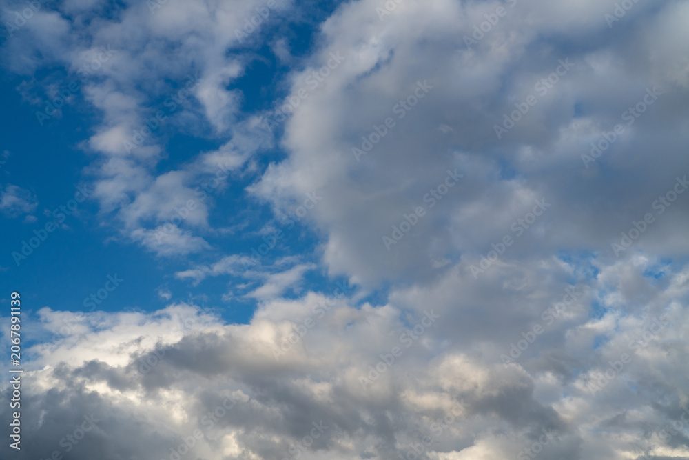 Fototapeta premium White clouds on a summer blue sky for background or wallpaper design. Majestic cumulus clouds float across the endless sky, their graceful forms painting a mesmerizing canvas of beauty and grandeur. 