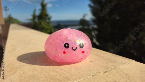 Schilderij op canvas Cute pink glitter dumpling squishy toy with a smiling face sitting on a sunny stone railing outdoors