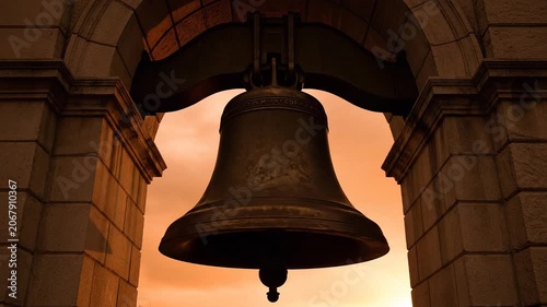 Large Antique Bronze Patriot Memorial Bell Hanging Inside an Old Stone Archway at Golden Sunset Hour