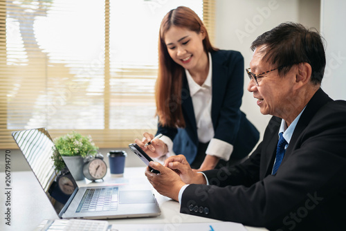 A man and a woman are sitting at a desk with a laptop and a cell phone