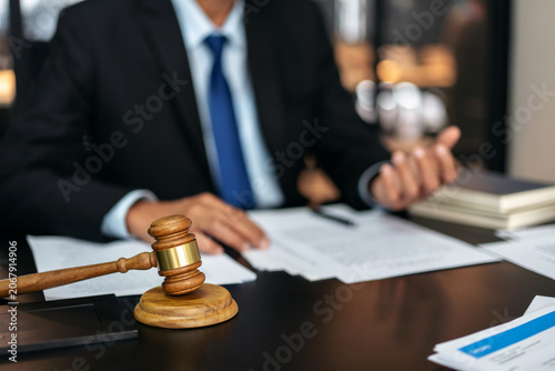 A man in a suit is sitting at a desk with a gavel and a stack of papers