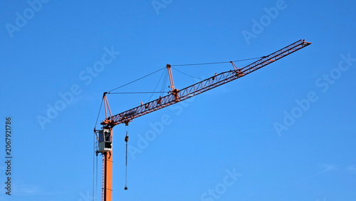 Konstfotografi Orange industrial tower crane with extended horizontal jib against a solid blue