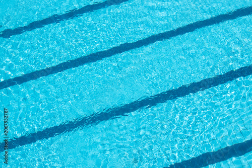 Top-down view of a blue-tiled outdoor swimming pool with crystal-clear water, shimmering and sparkling in the sun. Water texture background.