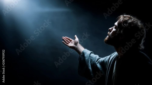Jesus reaching out in a moment of reflection in a dark setting with a light above him
