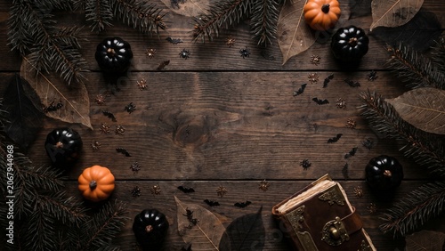 Halloween flat lay composition with rustic wooden background, pumpkins, pine branches, and antique book