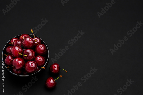 Fresh Cherries in Black Bowl on Dark Background. Top view of ripe sweet cherries in black bowl on dark background with copy space.