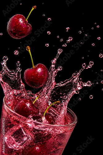 Fresh cherries creating splash in red juice with water droplets isolated on black background.