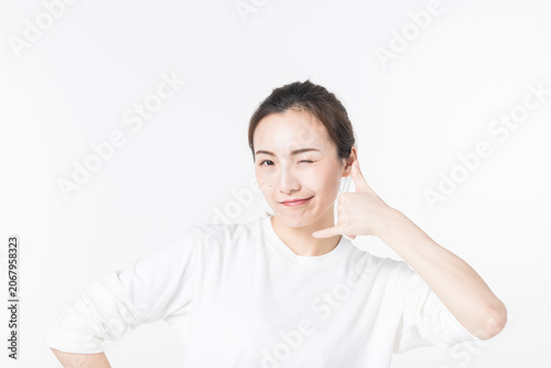 Foto Playful young woman winking with call me hand gesture on white background