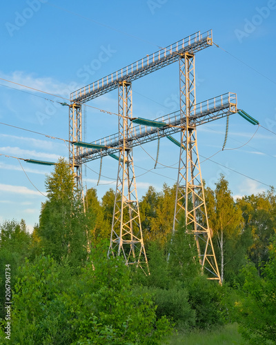 Foto High voltage power line gantry with insulators above forest edge under blue sky